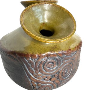 Puede incluir: Un jarr&oacute;n de cer&aacute;mica con una abertura ancha y acampanada y un esmalte marr&oacute;n y verde. El jarr&oacute;n tiene una superficie texturizada con un patr&oacute;n de espiral.
