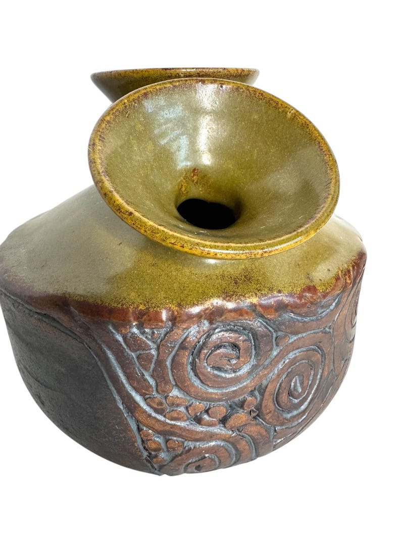 Puede incluir: Un jarr&oacute;n de cer&aacute;mica con una abertura ancha y acampanada y un esmalte marr&oacute;n y verde. El jarr&oacute;n tiene una superficie texturizada con un patr&oacute;n de espiral.