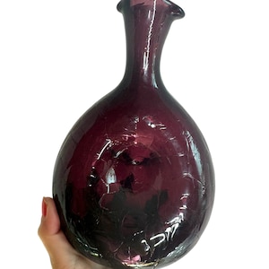 May include: A deep purple glass vase with a rounded body and a narrow neck. The vase has a textured surface.