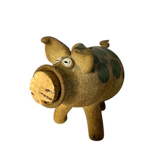 May include: A ceramic piggy bank with a cork stopper in its mouth. The pig is brown with green spots and has white eyes.