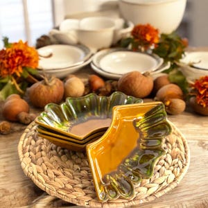 May include: A set of three ceramic dishes with a green and brown glaze. The dishes are stacked on top of each other and have a scalloped edge. The dishes are sitting on a woven wicker placemat.
