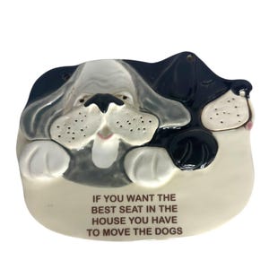 May include: A ceramic dog-shaped decorative piece in black, white, and gray. The dog's face is the focal point, with the text "IF YOU WANT THE BEST SEAT IN THE HOUSE YOU HAVE TO MOVE THE DOGS" below.