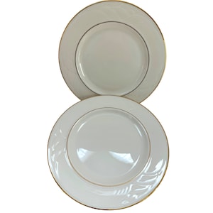 May include: Two white ceramic plates with a gold rim and a delicate floral design. The plates are stacked on top of each other.