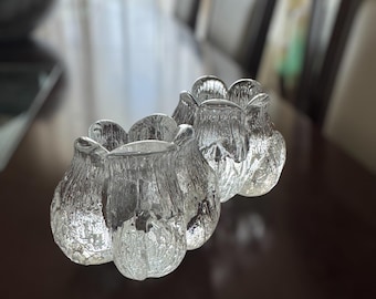 May include: Two clear glass candle holders with a textured, frosted finish. The holders are shaped like a flower with multiple petals.