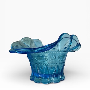May include: A vibrant blue glass bowl with a ruffled rim. The bowl features an intricate pattern of raised designs, including ovals, dots, and floral motifs. The bowl's base is scalloped, adding to its decorative appeal.