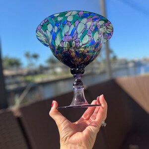 May include: A purple glass bowl with a stained glass design in shades of blue, green, and pink. The bowl is on a purple glass stem and base.
