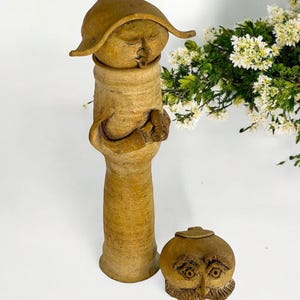 May include: Two ceramic figurines, one tall and slender with a hat and the other round with a face, both with a rustic brown glaze.