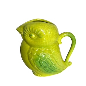 May include: A green ceramic pitcher shaped like a bird with a cracked glaze finish. The bird has a green wing and a yellow body.