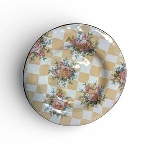 May include: Round decorative plate with a black rim. The plate features a yellow and white checkered pattern with floral rose bouquets. The roses are in shades of pink, peach, and yellow, with green leaves and small blue flowers.