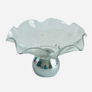 May include: A clear glass bowl with a wavy edge sits on a silver pedestal. The bowl has a star-shaped design etched into the glass.