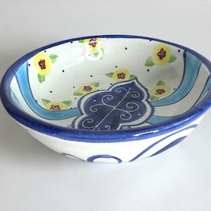 May include: A hand-painted ceramic bowl with a white interior, featuring yellow floral designs and a blue decorative pattern. The bowl has a blue rim and a light blue stripe design. The bowl is oval-shaped.
