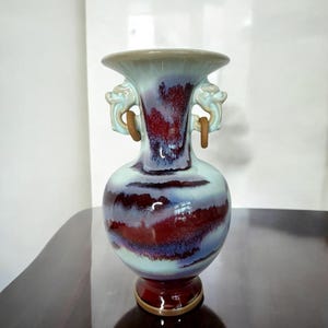 May include: A ceramic vase with a red and blue glaze and dragon handles. The vase has a round body and a flared top.