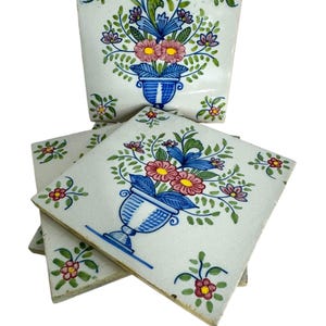 May include: Four antique ceramic tiles with a floral design. Each tile features a blue and white vase with pink and yellow flowers and green leaves.