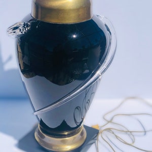 Puede incluir: Una l&aacute;mpara de mesa de vidrio negro con un elemento de dise&ntilde;o de vidrio transparente y una base de lat&oacute;n. La l&aacute;mpara tiene una base de m&aacute;rmol negro.
