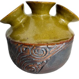 Puede incluir: Un jarr&oacute;n de cer&aacute;mica verde con tres aberturas, con una base marr&oacute;n y negra con un dise&ntilde;o de espiral.