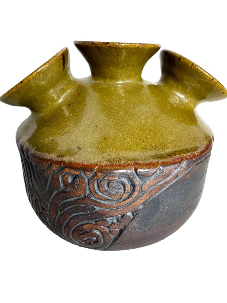 Puede incluir: Un jarr&oacute;n de cer&aacute;mica verde con tres aberturas, con una base marr&oacute;n y negra con un dise&ntilde;o de espiral.