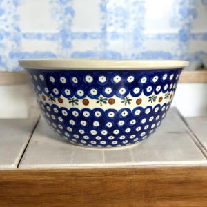 May include: A blue and white ceramic mixing bowl with a brown and green floral pattern around the rim. The bowl has a white interior and is decorated with a polka dot pattern.