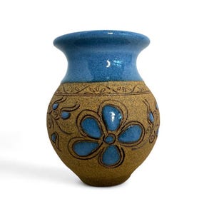 May include: A small, hand-crafted ceramic vase with a blue glaze and a brown, textured body. The vase is decorated with a blue floral design.