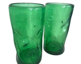 May include: Two green, hand-blown drinking glasses. The glasses have a textured, crackled appearance and a slightly curved shape. The vibrant green colour and unique texture give them a rustic, artisanal feel. Ideal for serving water, juice, or cocktails.