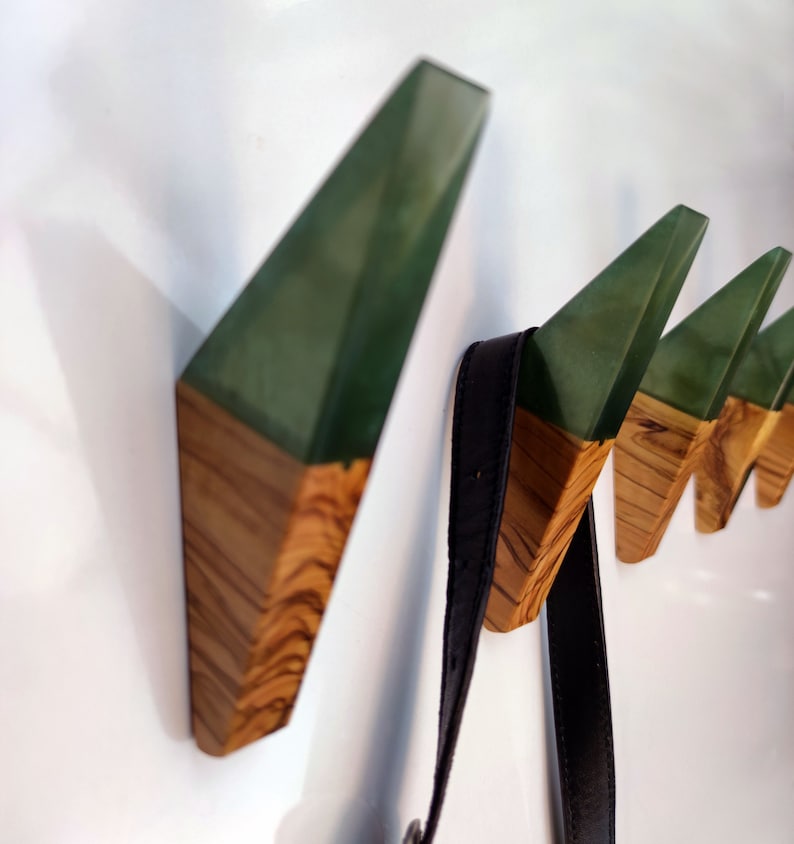 May include: A set of five wall hooks made of wood and green resin. The hooks are shaped like triangles and have a modern design.