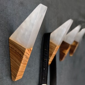 May include: Four white resin and wood wall hooks in a triangular shape. The hooks are mounted on a gray wall.