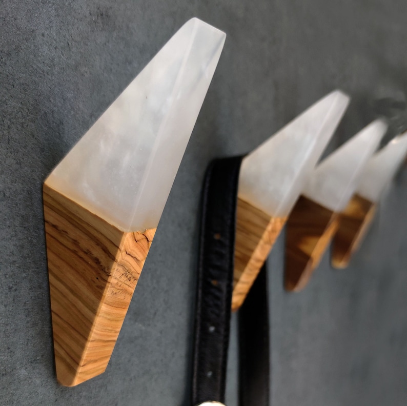 May include: Four white resin and wood wall hooks in a triangular shape. The hooks are mounted on a gray wall.