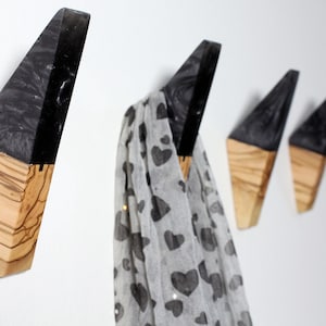Puede incluir: Un conjunto de cuatro perchas de pared de madera con un dise&ntilde;o geom&eacute;trico. La parte superior es negra y la inferior de madera natural. Una bufanda con estampado de corazones cuelga.
