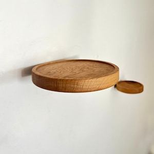 May include: Two round wooden shelves mounted on a white wall. The larger shelf is in the foreground and the smaller shelf is in the background.