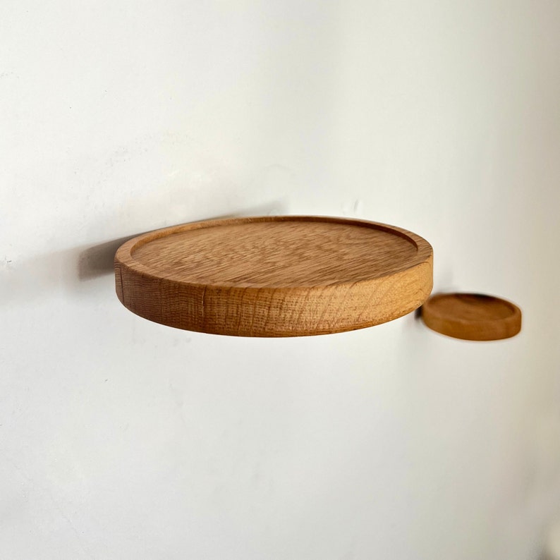 May include: Two round wooden shelves mounted on a white wall. The larger shelf is in the foreground and the smaller shelf is in the background.