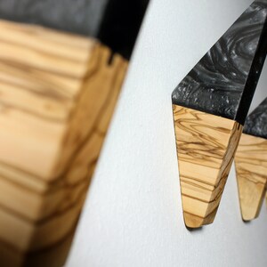 Puede incluir: Ganchos de pared de madera con dise&ntilde;o geom&eacute;trico. Cada gancho tiene una base de madera clara y una parte superior oscura y veteada. Montados en una pared blanca, resaltan su forma y textura &uacute;nicas. El dise&ntilde;o es moderno y minimalista, adecuado para cualquier interior.