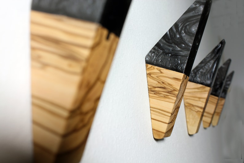 Puede incluir: Ganchos de pared de madera con dise&ntilde;o geom&eacute;trico. Cada gancho tiene una base de madera clara y una parte superior oscura y veteada. Montados en una pared blanca, resaltan su forma y textura &uacute;nicas. El dise&ntilde;o es moderno y minimalista, adecuado para cualquier interior.