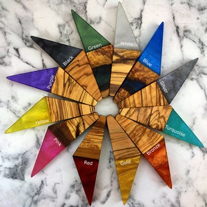 Puede incluir: Una colecci&oacute;n de piezas triangulares de madera y resina dispuestas en un patr&oacute;n circular. Cada pieza presenta una secci&oacute;n de madera de olivo y una punta de resina coloreada, con colores como negro, verde, blanco, azul, plata, turquesa, bronce, oro, rojo, rosa, amarillo y morado.