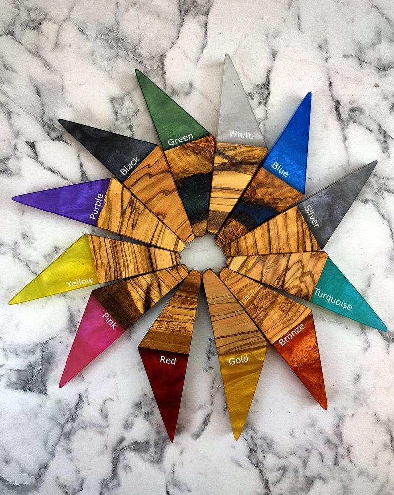 Puede incluir: Una colecci&oacute;n de piezas triangulares de madera y resina dispuestas en un patr&oacute;n circular. Cada pieza presenta una secci&oacute;n de madera de olivo y una punta de resina coloreada, con colores como negro, verde, blanco, azul, plata, turquesa, bronce, oro, rojo, rosa, amarillo y morado.