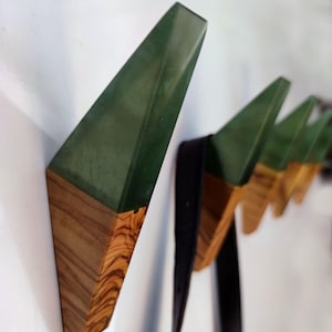 May include: A set of five wall hooks made of wood and green resin. The hooks are shaped like triangles and have a modern design.