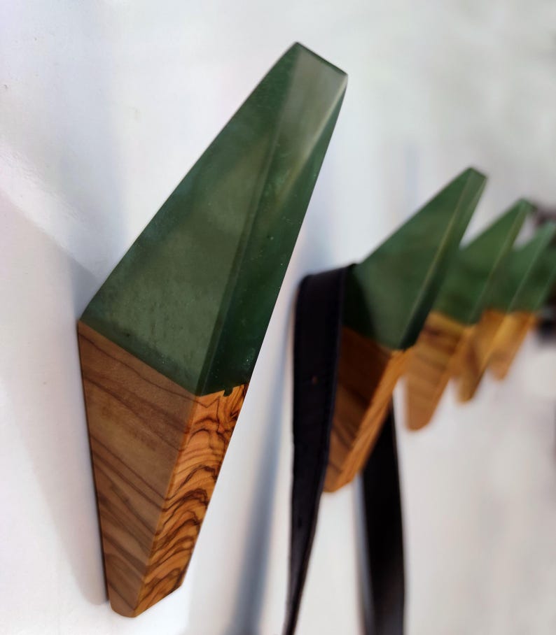 May include: A set of five wall hooks made of wood and green resin. The hooks are shaped like triangles and have a modern design.