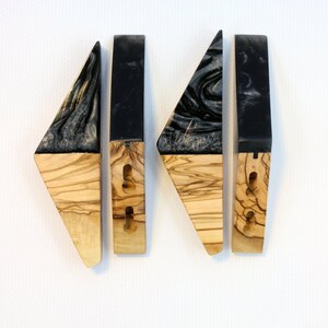Puede incluir: Cuatro tiradores de armario de madera hechos a mano. Cada tirador presenta una secci&oacute;n de madera de olivo y una parte superior de resina negra con un patr&oacute;n gris arremolinado. Los tiradores tienen agujeros pretaladrados para una f&aacute;cil instalaci&oacute;n.