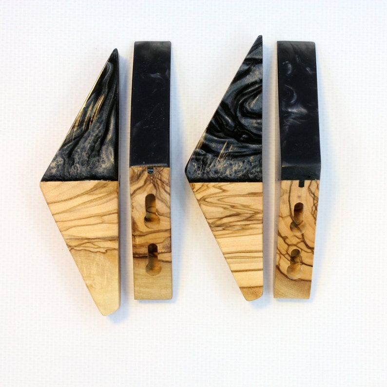 Puede incluir: Cuatro tiradores de armario de madera hechos a mano. Cada tirador presenta una secci&oacute;n de madera de olivo y una parte superior de resina negra con un patr&oacute;n gris arremolinado. Los tiradores tienen agujeros pretaladrados para una f&aacute;cil instalaci&oacute;n.