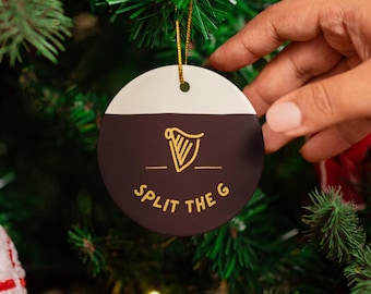 May include: A circular Christmas tree decoration with a gold string, held by a hand. The ornament is half white and half dark brown, with a gold harp design and the words "SPLIT THE G". The text "PERSONALIZE WITH A NAME!" is at the bottom.