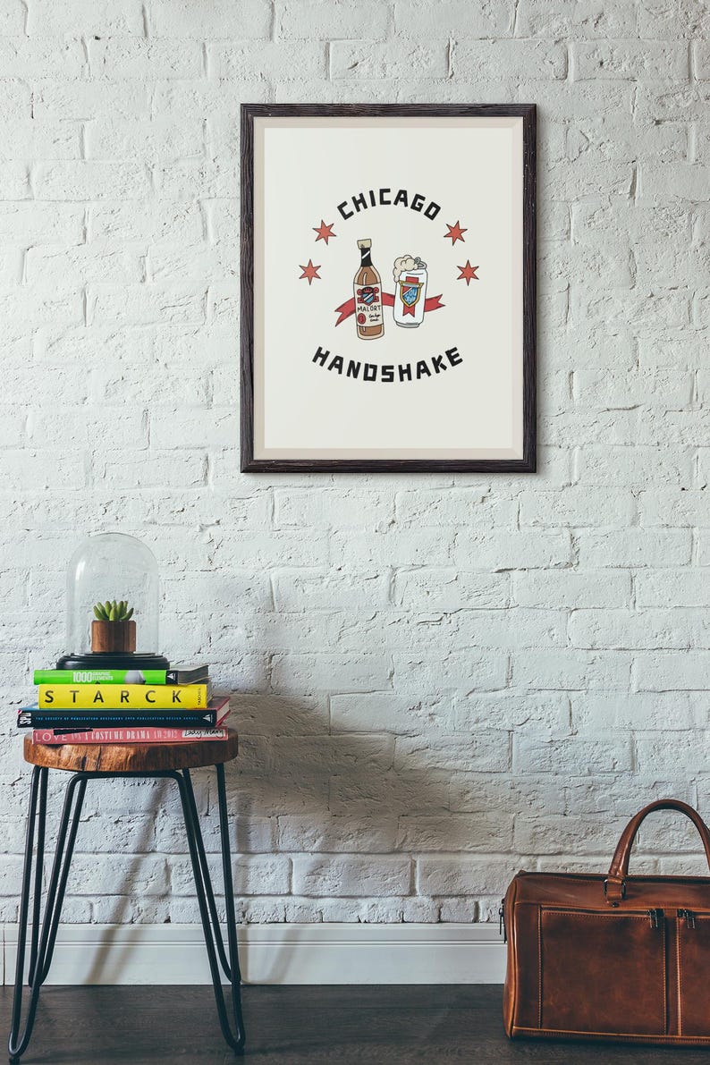 May include: A framed print with a white background and a black border. The print features a cartoon illustration of a bottle of Mal&ouml;rt and a glass of beer with the text "Chicago Handshake" and five red stars.