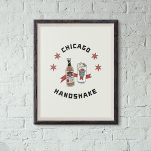 May include: A framed print with a white background and black text that reads "CHICAGO HANDSHAKE". The print features a cartoon illustration of a bottle of Mal&ouml;rt liquor and a can of beer.