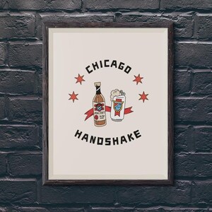 A framed Chicago Handshake art print hangs on a dark gray painted brick wall.