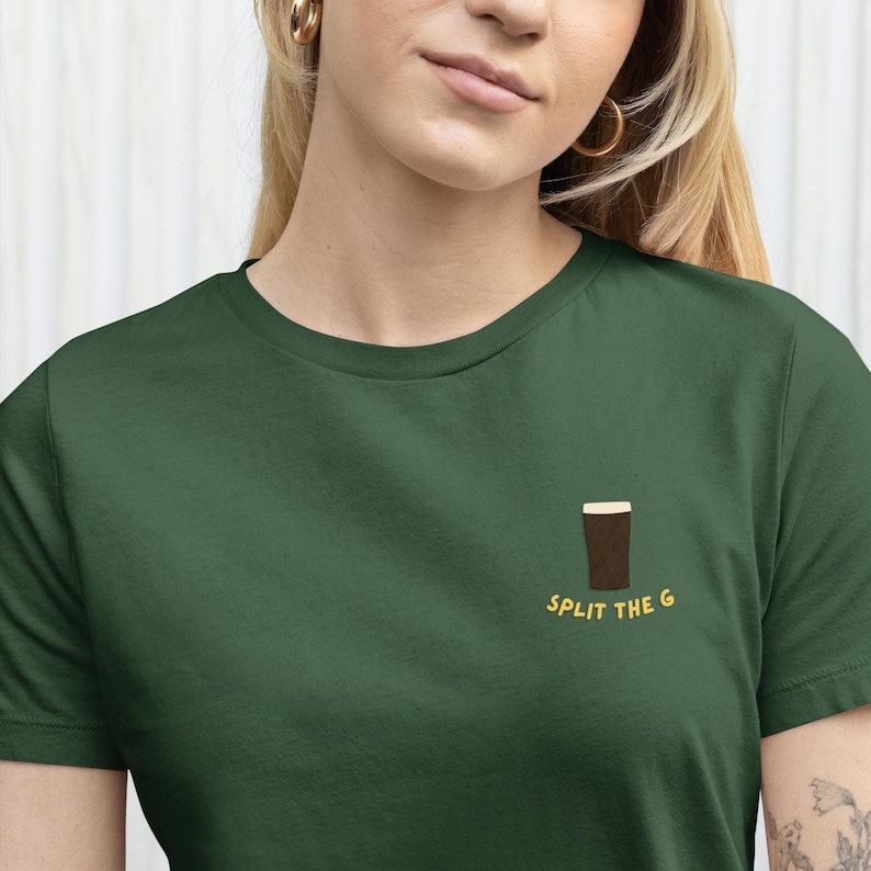 May include: Dark green t-shirt with a small embroidered pint of stout. The text "SPLIT THE G" is in yellow below the pint. The shirt is made of a soft material.