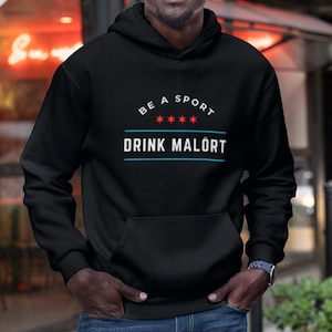May include: Black hooded sweatshirt with the text "Be a Sport Drink Malört" in white and red lettering with a blue and white border. The text is surrounded by five red stars.