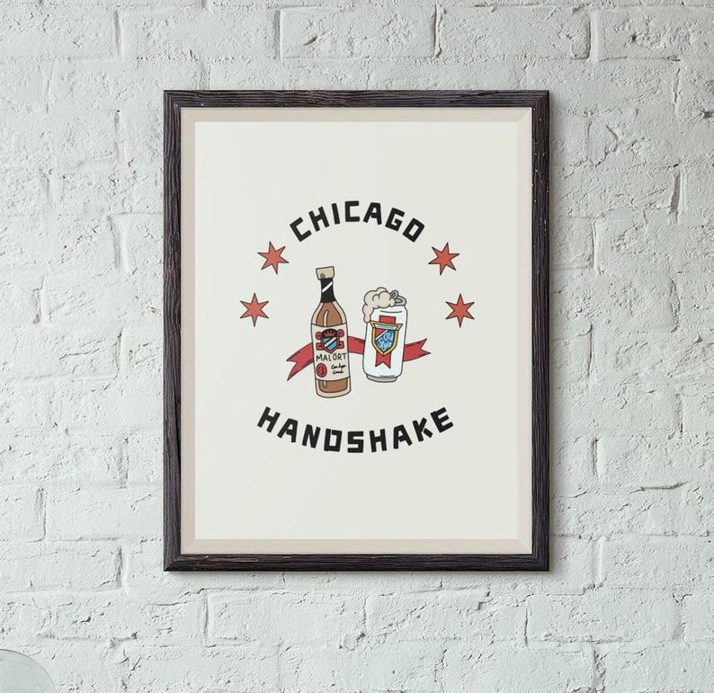 A framed Chicago Handshake art print hangs on a white painted brick wall.