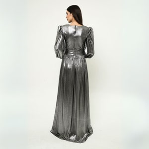 May include: A silver metallic maxi dress with long sleeves and a fitted bodice. The dress has a gathered skirt and a V-neckline.