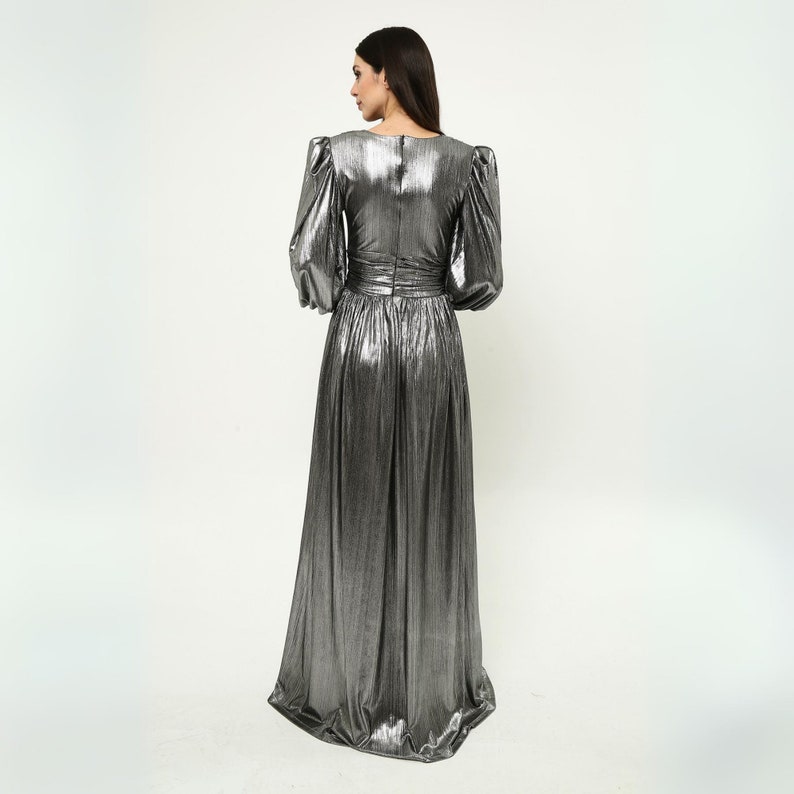 May include: A silver metallic maxi dress with long sleeves and a fitted bodice. The dress has a gathered skirt and a V-neckline.