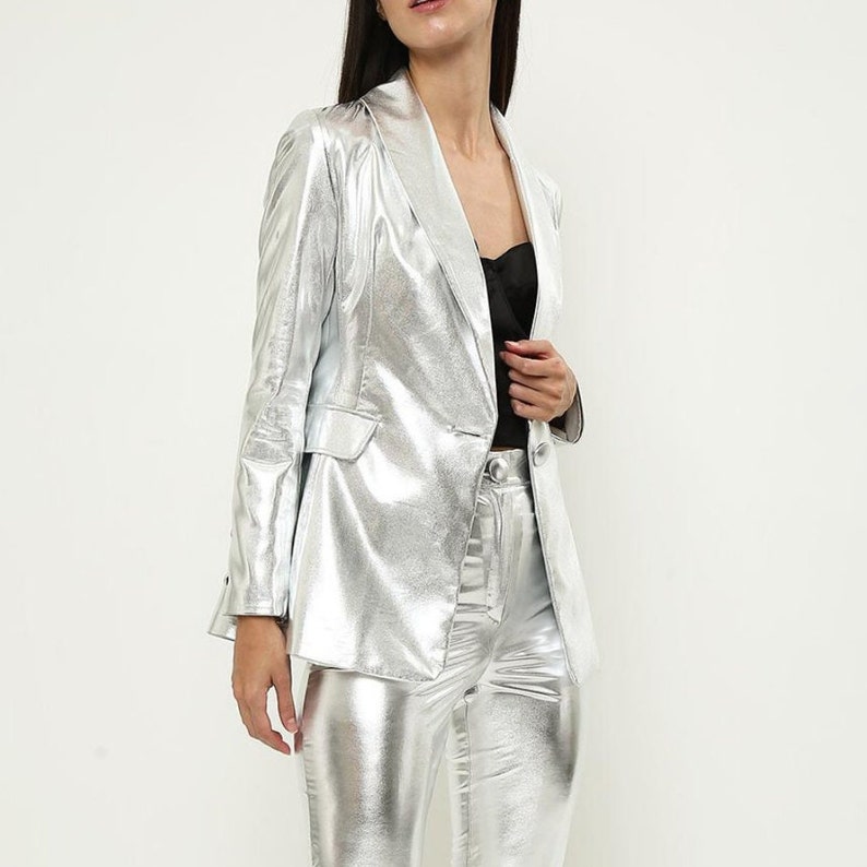 May include: A silver metallic blazer and pants set. The blazer has a single button closure and a notched collar. The pants are slim fitting.