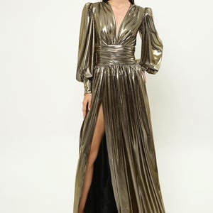 May include: A long, gold metallic dress with a plunging neckline, long sleeves, and a thigh-high slit. The dress has a fitted bodice and a flowing skirt.