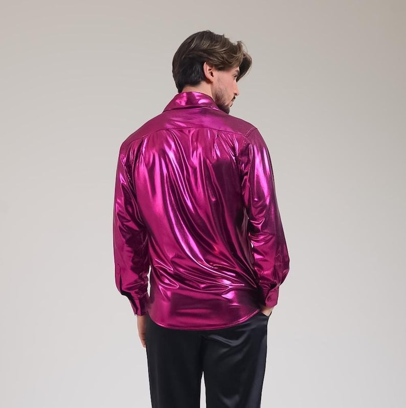 K&ouml;nnte beinhalten: Ein gl&auml;nzendes, magentafarbenes Langarmhemd mit klassischem Kragen. Das Hemd hat ein gl&auml;nzendes, metallisches Finish und wird mit einer schwarzen Hose kombiniert. Der Stoff reflektiert das Licht und erzeugt einen lebendigen und auff&auml;lligen Look.