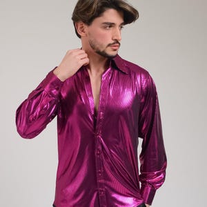 K&ouml;nnte beinhalten: Ein lang&auml;rmeliges, gekn&ouml;pftes Hemd in leuchtendem Magenta. Das Hemd hat ein gl&auml;nzendes, metallisches Finish, einen klassischen Kragen und gekn&ouml;pfte Manschetten. Das Hemd ist oben aufgekn&ouml;pft und gibt die Brust frei.